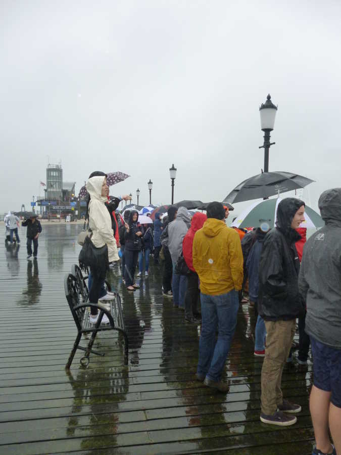 Photograph of spectators, with umbrellas and raincoats, at the end of Southend Pier.